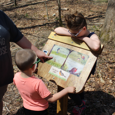 StoryWalk image showing two kids looking at the book display on the trail