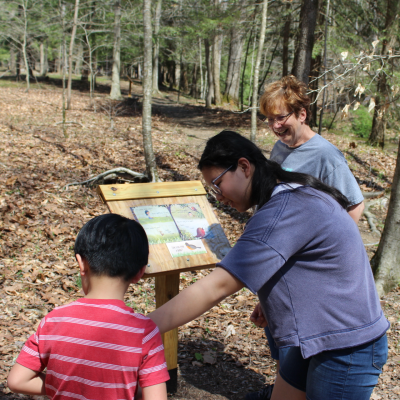 StoryWalk image showing two women and a boy looking at one of the book displays on the walk trail