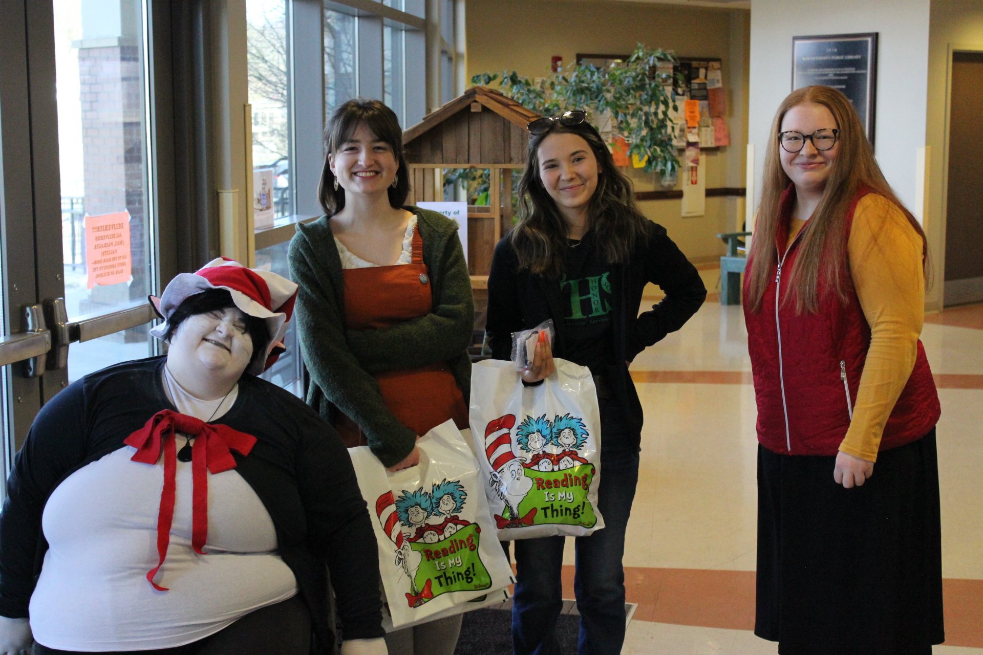 Teen volunteers holding Dr. Seuss bags beside wheelchair user dressed as Dr. Seuss's the Cat in the Hat