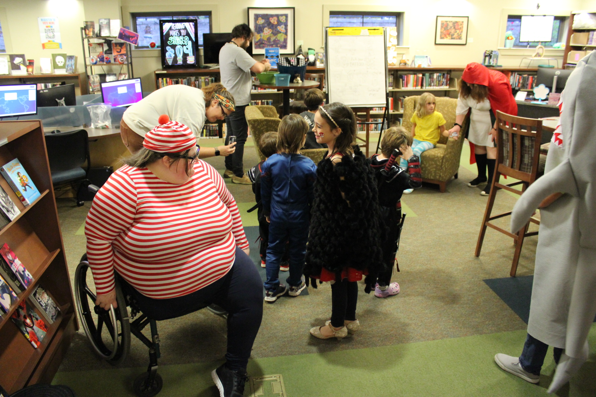 Costumed children in library children's area with patron in wheelchair dressed as Waldo in foreground