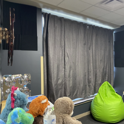 Room interior in dark colors with curtained window, kinetic sculpture, sound-dampening foam panels on walls, and brightly-colored stuffed toys and beanbag chair