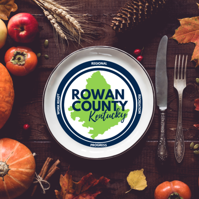 Table decorated with pumpkins, pomegranates, and persimmons with silverware and plate holding Rowan County Kentucky logo
