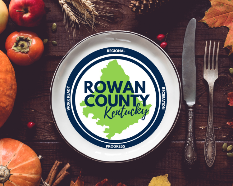 Table decorated with pumpkins, pomegranates, and persimmons with silverware and plate holding Rowan County Kentucky logo