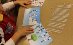 Child using sticky rhinestones to spell words in braille on illustrated cards